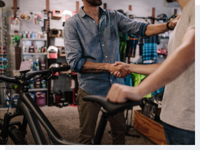A bicycle shop owner shaking hands with a male customer who just purchased a bike