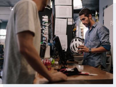 A cashier standing the cash register looking up information on a cycling helmet for the male customer at the register with him