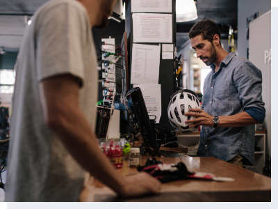 Customer purchasing bicycle helmet A cashier standing the cash register looking up information on a cycling helmet for the male customer at the register with him