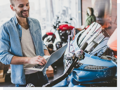 A man standing in a motorcycle shop with his laptop while looking a bike